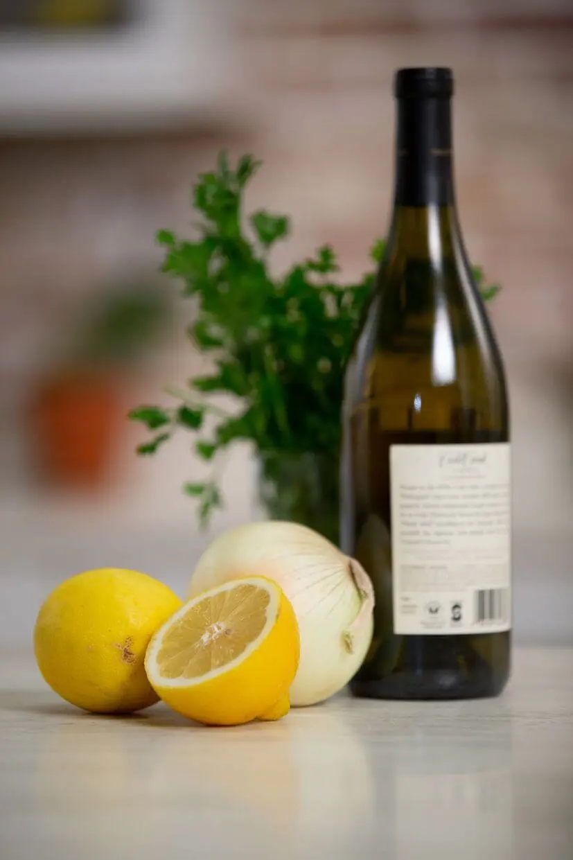 A bottle of white wine on a countertop beside fresh lemon, onion, and parsley.