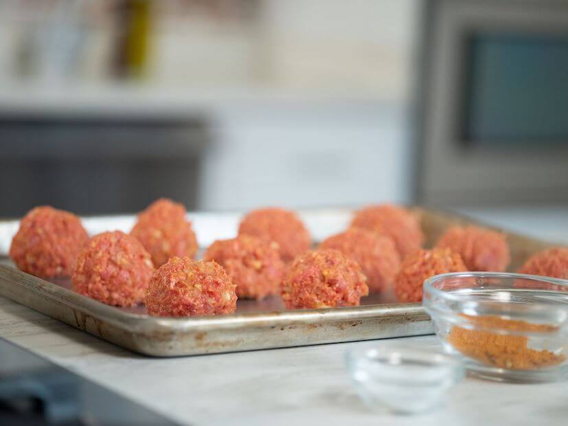 Uncooked meatballs sitting in a silver baking pan 