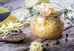 Homemade sauerkraut in a glass jar with caraway seeds and juniper berries on a rustic table.