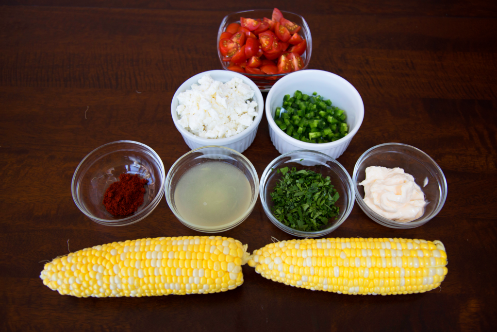 Summer corn salad ingredients: corn, feta, paprika, cilantro, jalapeno, lime juice, mayonnaise and tomatoes.