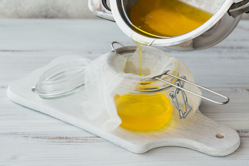Clarified butter being poured into a glass jar 